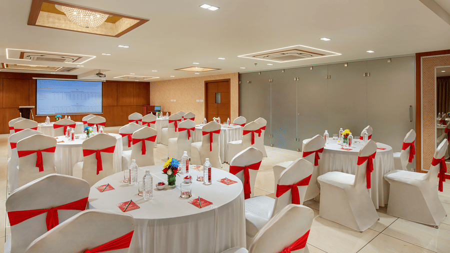 A brightly lit banquet hall set up with round tables and decorated chairs, ready for an event - SK Lords Inn Ahmedabad