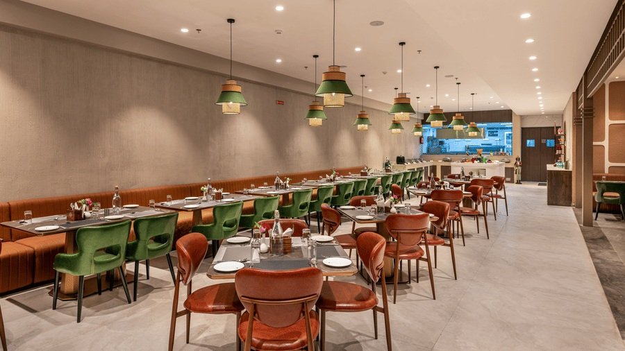 A stylish view of Blue Coriander restaurant featuring elegant emerald green and orange seating, tables, and warm pendant lighting – Skkylight Lords Inn, Nanded