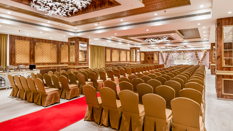 Full view of the Raj Mahal hall featuring rows of elegant chairs covered with golden cloth, a vibrant red carpet aisle, and a spacious stage area – Skkylight Lords Inn, Nanded