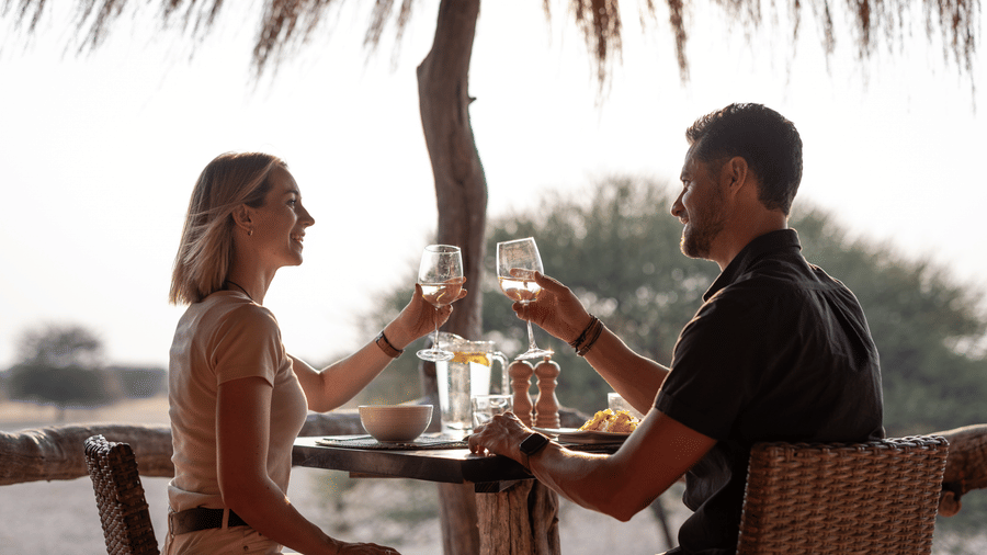 Couple toasting drinks over an intimate bush dining experience at Evolve Back Kalahari
