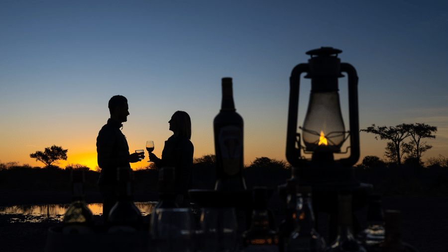 Silhouette of guests with lanterns enjoying a sundowner at Kalahari sunset at Evolve Back resort