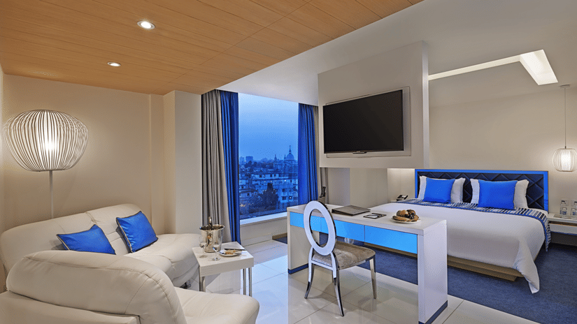 A Superior Room at Barsana Boutique Hotel, Kolkata, featuring a modern couch and a plush bed placed next to a large window offering city views from the room.