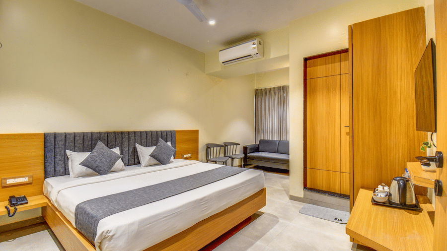 Executive Room at VITS Select Nashik Hotels & Resorts featuring a plush bed facing the TV on the wall under which a tea and coffee maker is placed on a wooden surface