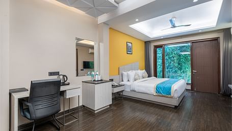 A spacious room at DLS Forest Vines Resort featuring a large bed, glass windows, a desk, and a chair.