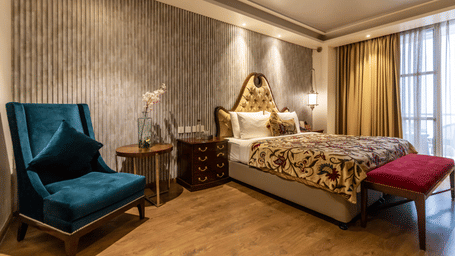 A bedroom with a king size bed, armchair, side tables, lamps, and curtains inside at Indraprastha Resort & Spa, McLeod Ganj.