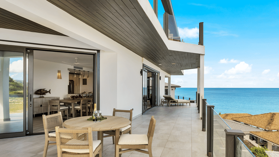 A balcony with a sea view at Tamarind Hills Resort and Villas, Antigua, with a table, four chairs and a glass sliding door leading to a room.