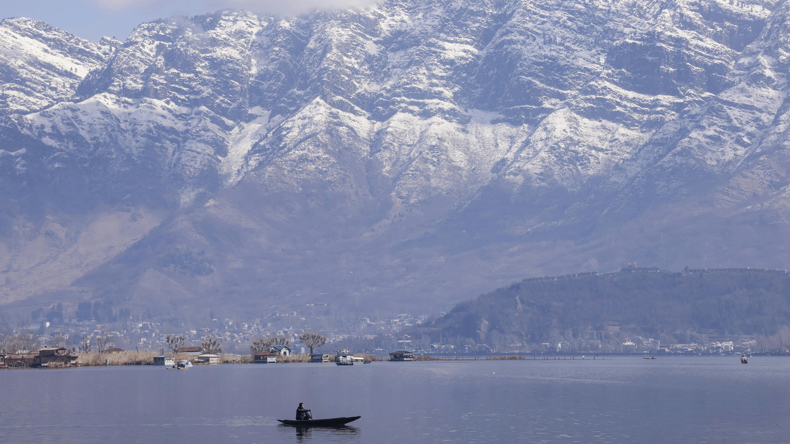 A serene lake with a small boat floating and snow-covered mountains in the background.