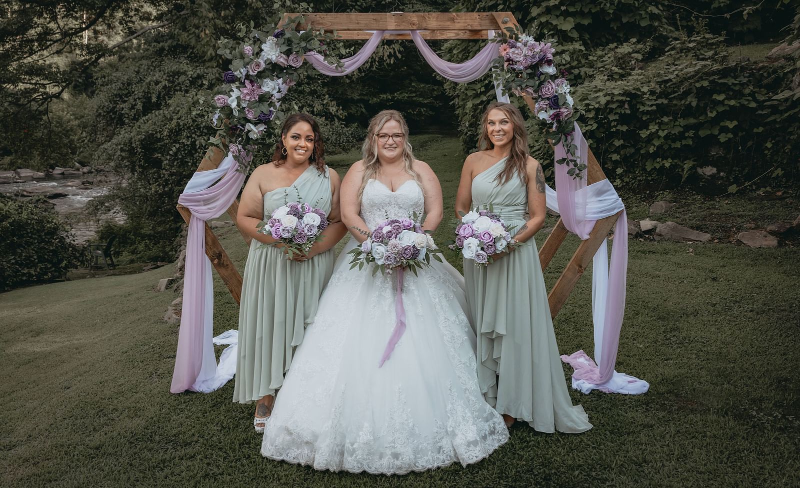 Bride standing next to her bridesmaids with bouquets in their hands in front of the wooden frame decorated with flowers at the Historic Tapoco Lodge.