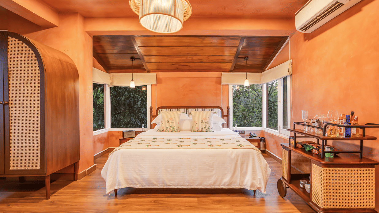 View of the Penthouse at Unseen Boutique Hotel Assagao Goa with a king bed, rattan pendant light, wooden ceiling, and warm natural light.
