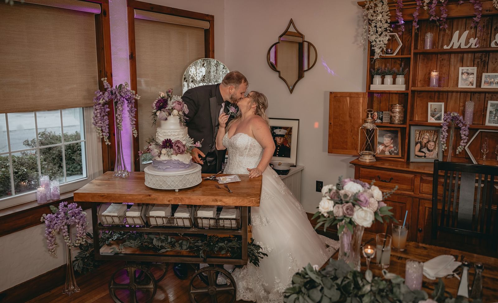 Just married couple kissing each other in one of the rooms of the Historic Tapoco Lodge. Near them there is a table with chairs which has a multi layer cake for wedding celebration.