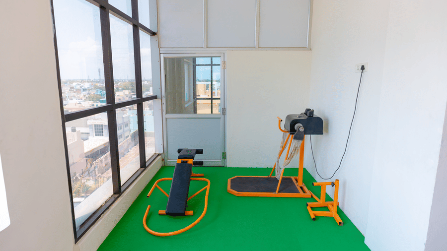 Fitness area at DSF Grand Plaza, Tuticorin with a green rubber floor, a sit-up bench, and a cable machine beside floor-to-ceiling windows overlooking the city.