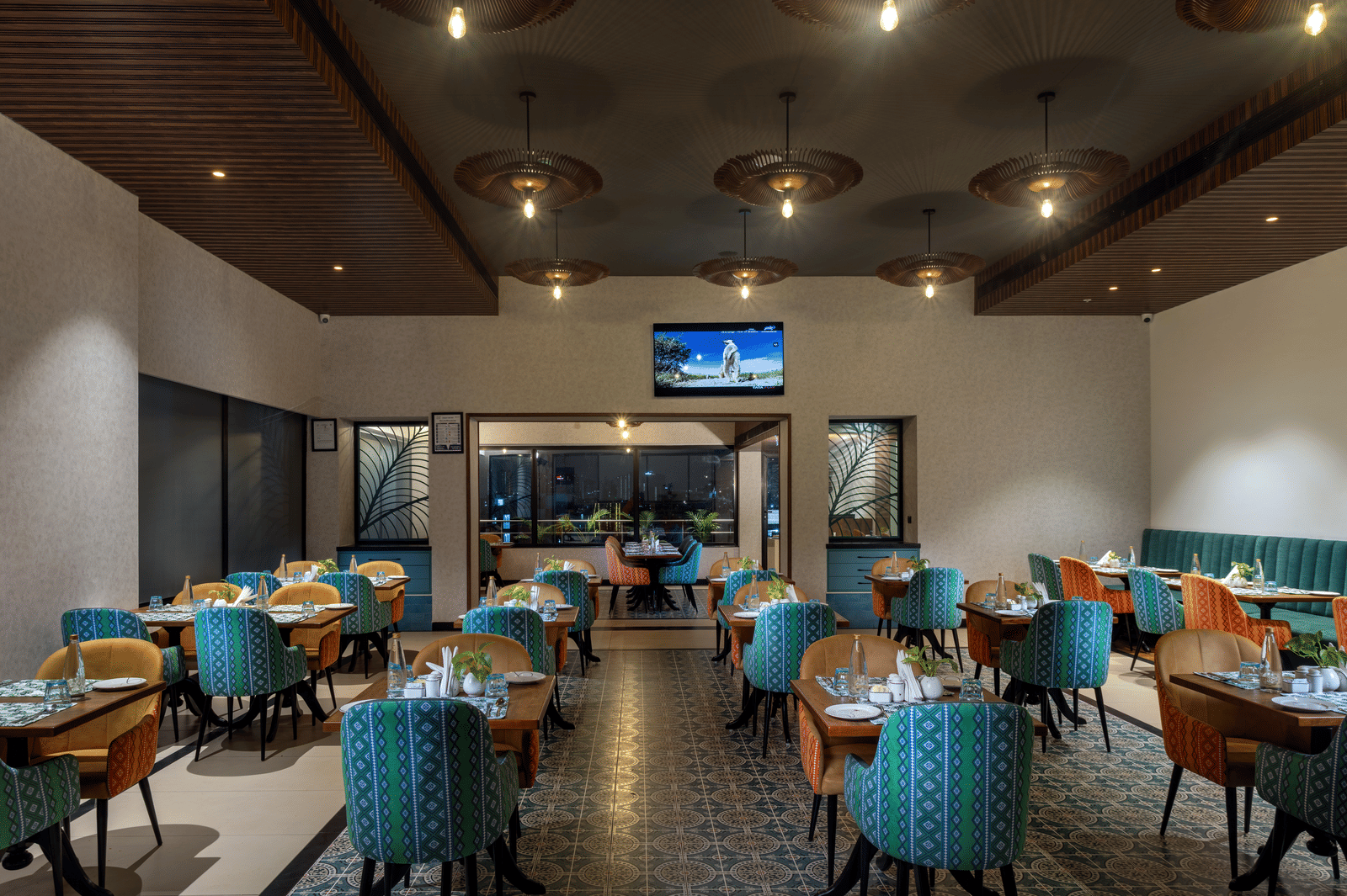 Cosy indoor dining area at Shalimar, the best restaurant in Hyderabad, with patterned flooring, a central TV, and ambient lighting | Zibe Luxe Hyderabad by GRT Hotels