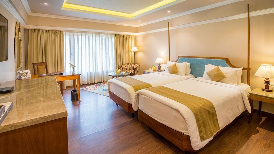Spacious bed with a wall-mounted TV opposite it and a large window covered by curtains.