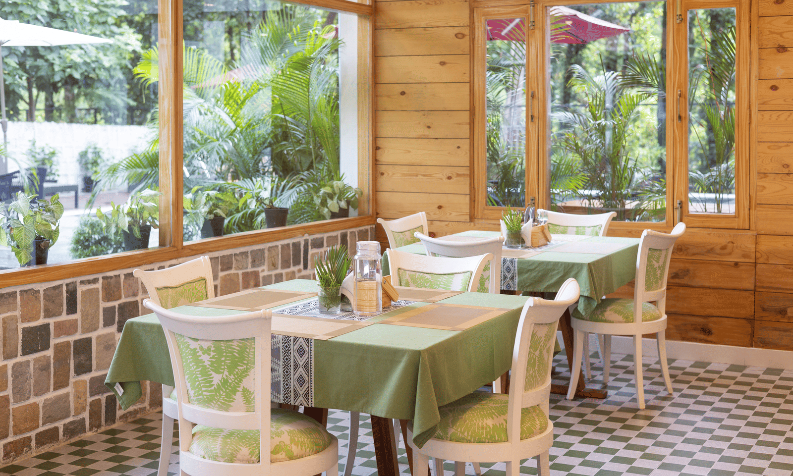 A brightly lit restaurant interior features wooden beams and large windows overlooking a lush garden - Megha Resort & Villas, Dehradun