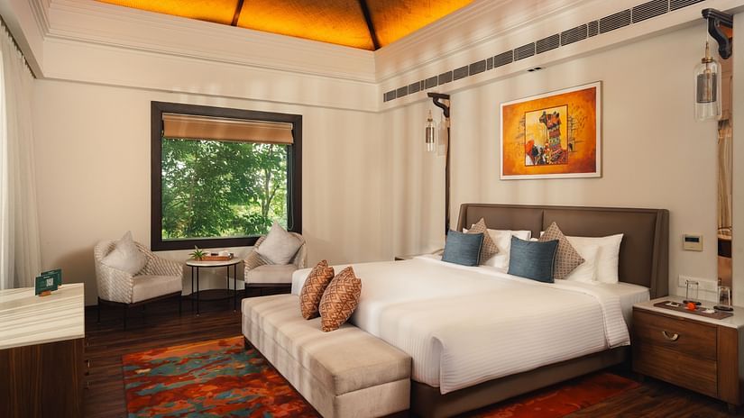 A hotel bedroom with a large bed, seating area by the window, and warm lighting.