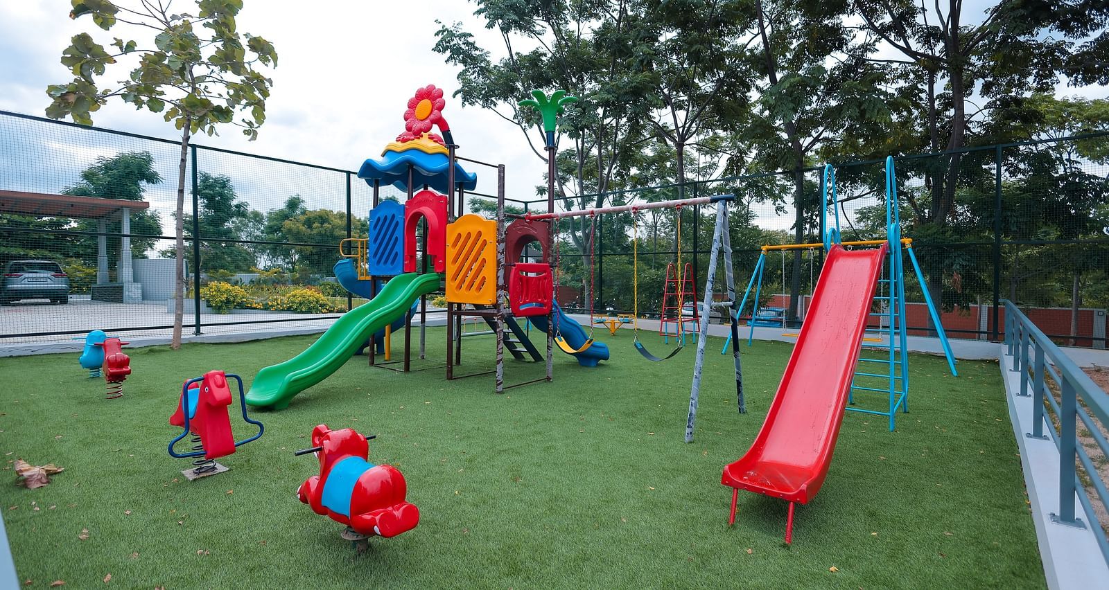 Outdoor kids play area at Trishvam Symphony, Krishnagiri, featuring colourful slides, climbing frames, and soft green turf.