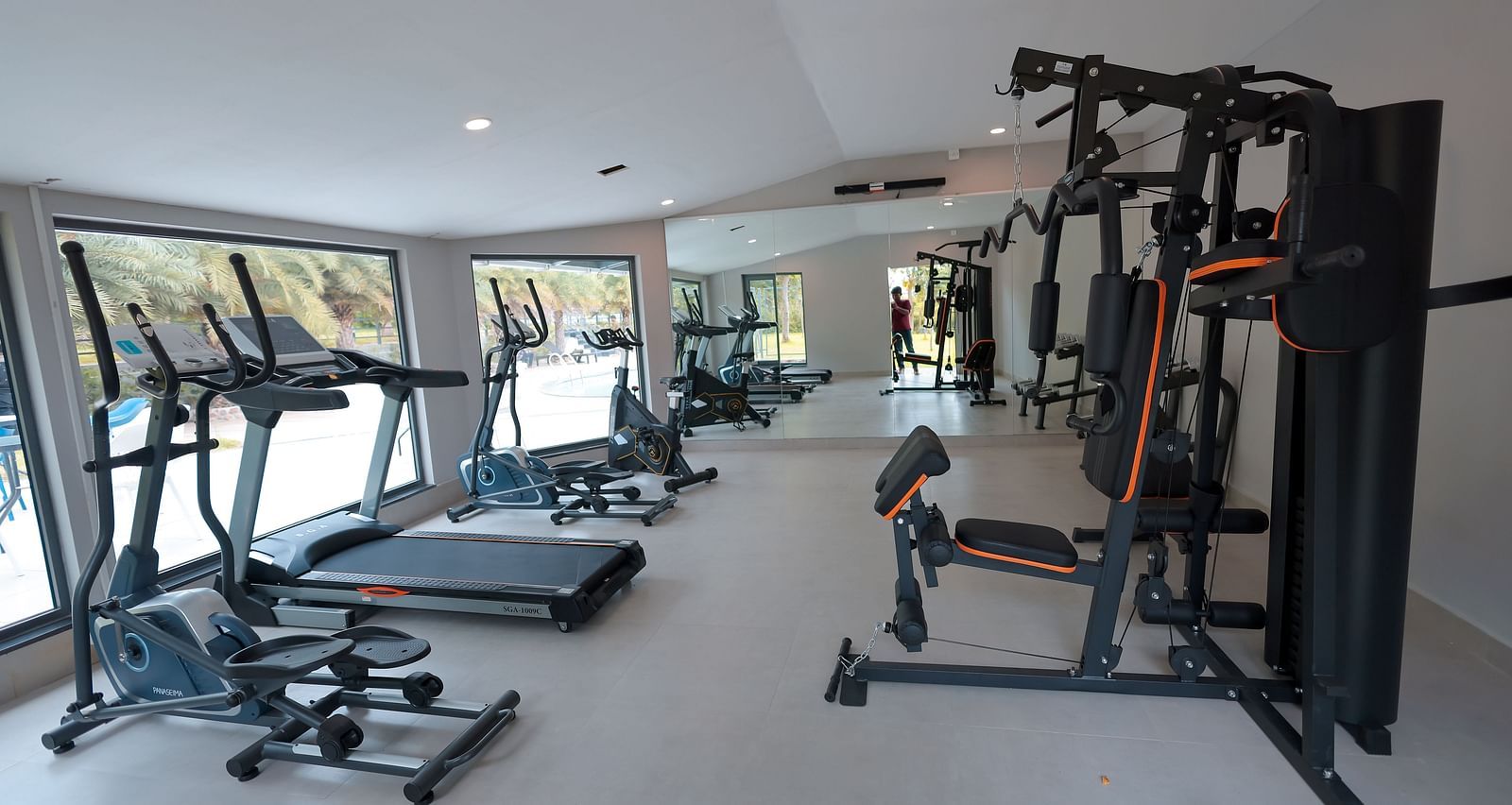 Indoor gym with weight machines, mirrors, and windows at Trishvam Symphony, Krishnagiri.