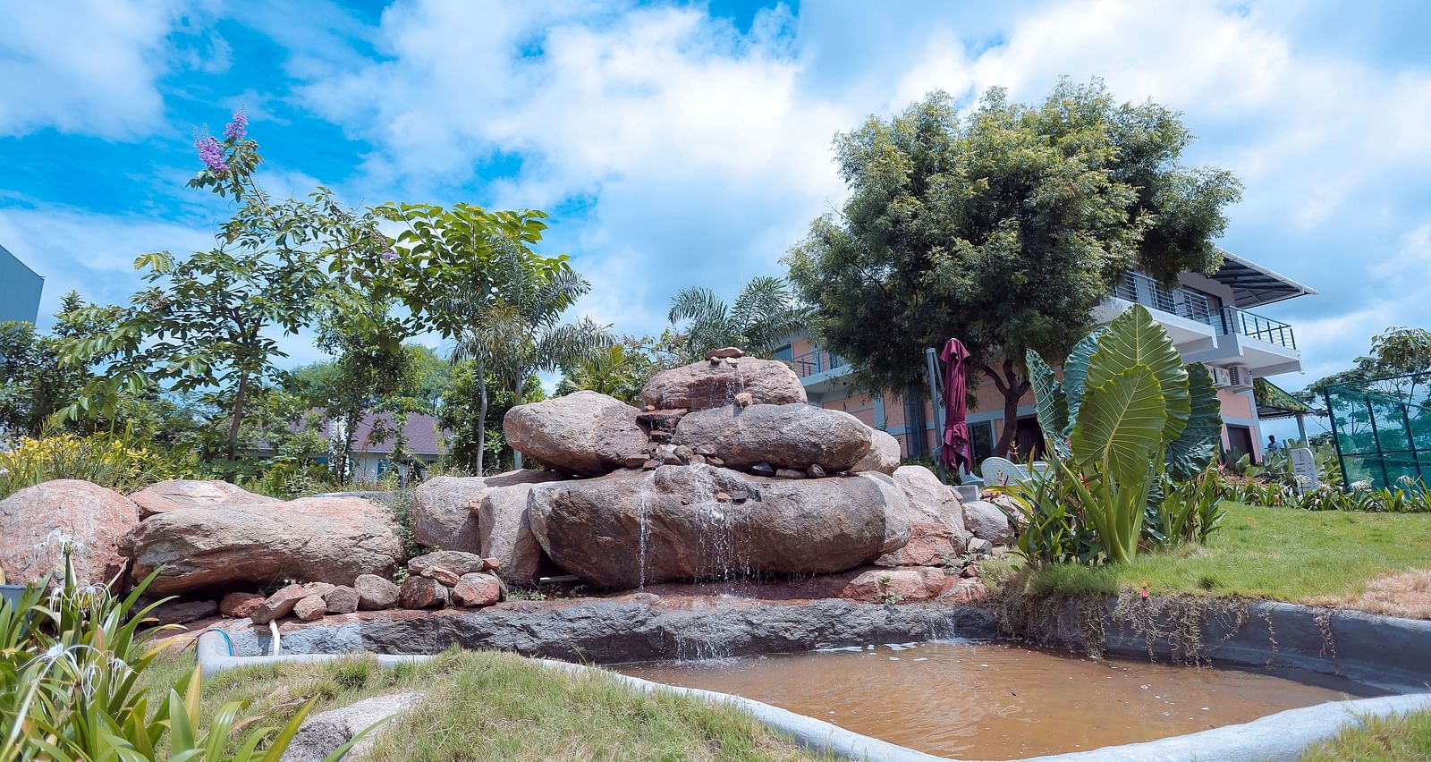 Rock waterfall feature surrounded by landscaped greenery at Trishvam Symphony, Krishnagiri.