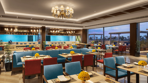 A large restaurant at Sarovar Portico, Hanumangarh, with blue and red chairs, tables, and a buffet area.