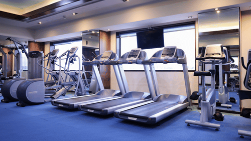A gym with treadmills, elliptical machines, and fitness equipment, with large windows and mirrors - Balaji Sarovar Premiere, Solapur