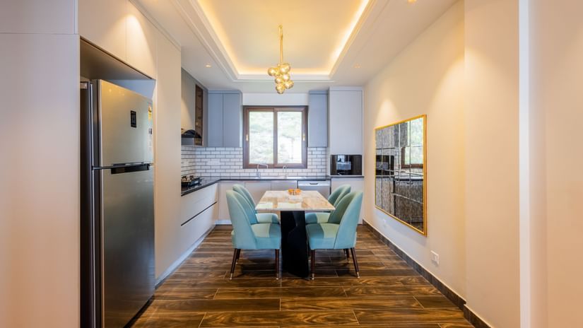 Spacious dining area featuring neatly arranged tables set with plates, cutlery, glasses, and napkins, surrounded by comfortable seating and warm, contemporary decor with natural light at The Manor Luxury Apartments, Shimla.