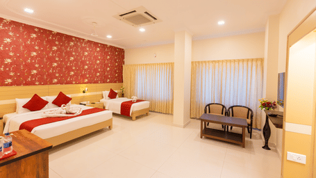 Club Room at DSF Grand Plaza, Tuticorin with a double bed and single bed, red floral wallpaper, red bed runners with a towel swan display, and a small seating area.