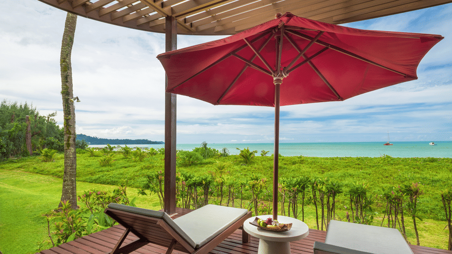 An outdoor deck area of Oceanfront Villa with lounge chairs, a shaded umbrella, and open views of surrounding greenery at Ramada Resort.