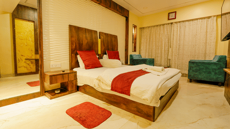 A bedroom with a king size bed, red cushions, a mirror, a bedside table and 2 armchairs at Hotel Seagull Digha.