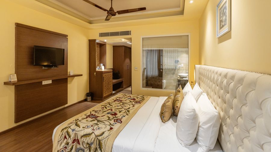 A bedroom with a king size bed, cushions, wall-mounted TV, side tables, and a wardrobe  at Indraprastha Resort & Spa, McLeod Ganj.