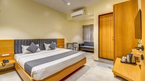 Executive Room at VITS Select Nashik Hotels & Resorts featuring a plush bed facing the TV on the wall under which a tea and coffee maker is placed on a wooden surface