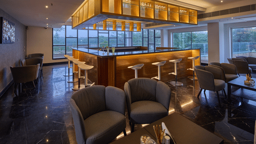 two chairs in front of the bar area with bar stools next to it at unwind kitchen and bar at Grand Continent, Mahabalipuram 