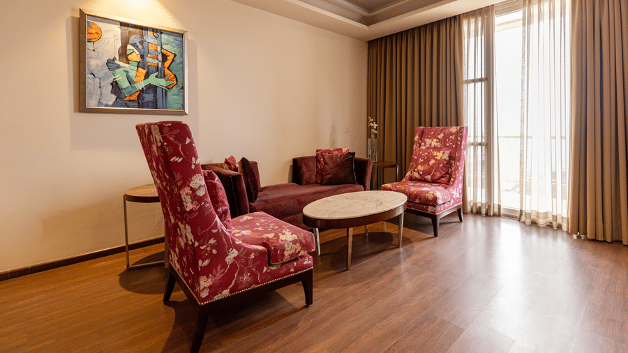 A seating area with 2 armchairs, sofa, table, curtains, and wall art arranged indoors at Indraprastha Resort & Spa, McLeod Ganj.