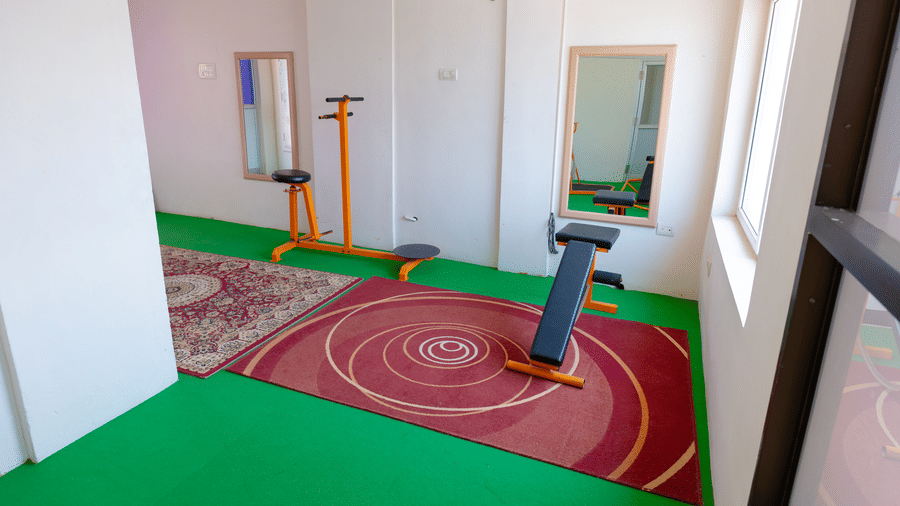 Gym corner at DSF Grand Plaza, Tuticorin with a green rubber floor, patterned rugs, an adjustable exercise bench, and wall mirrors.