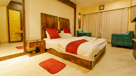 A bedroom with a king size bed, red cushions, a mirror, a bedside table and 2 armchairs at Hotel Seagull Digha.