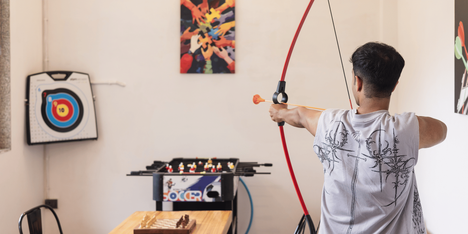 An individual is engaging in archery practice indoors, aiming at a target in a recreation room at Megha Resort & Villas, Dehradun.