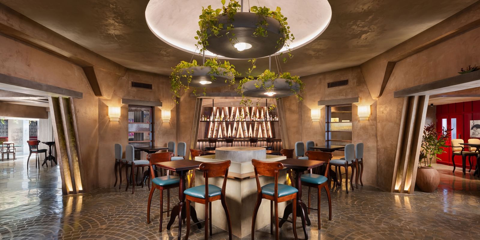 A bar area at Shilton International, Kochi, with a central round bar, stools, and hanging plant decorations.