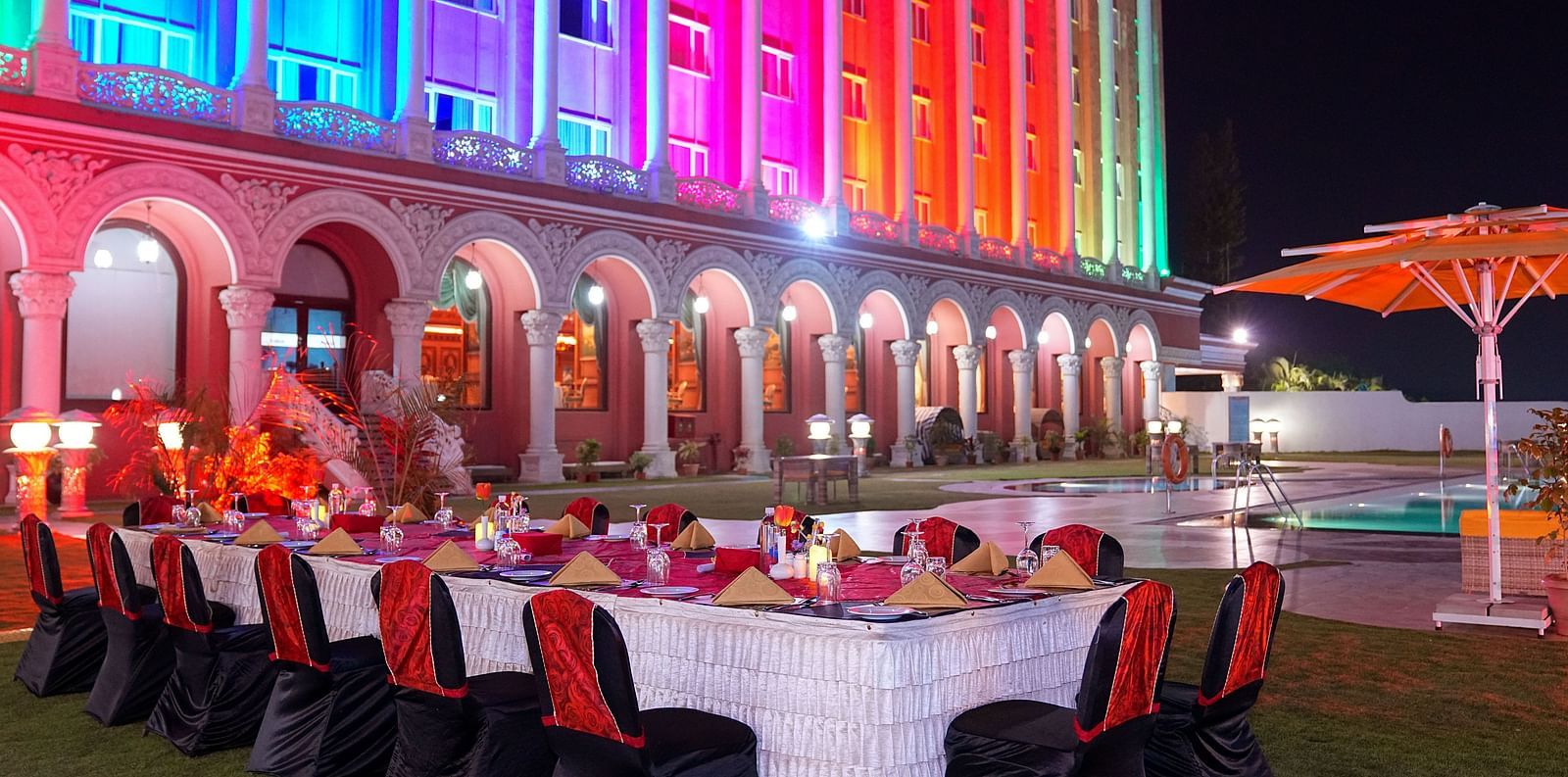 a long banquet table with plates and candles on top of it with Sitara Luxury Hotel in the background - Ramoji Film City Hotels - Hyderabad 