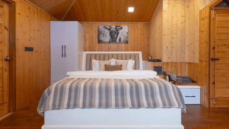 A cosy bedroom features wooden walls and a double bed with a striped neutral-toned coverlet at Megha Resort & Villas, Dehradun.