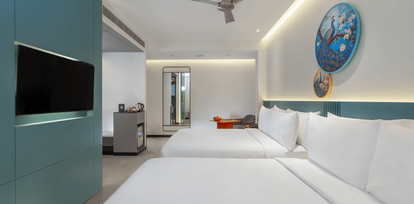 A hotel room featuring two large beds, a wall-mounted television, a ceiling fan, and a minibar at Zibe Luxe | Best Hotels to stay in hyderabad