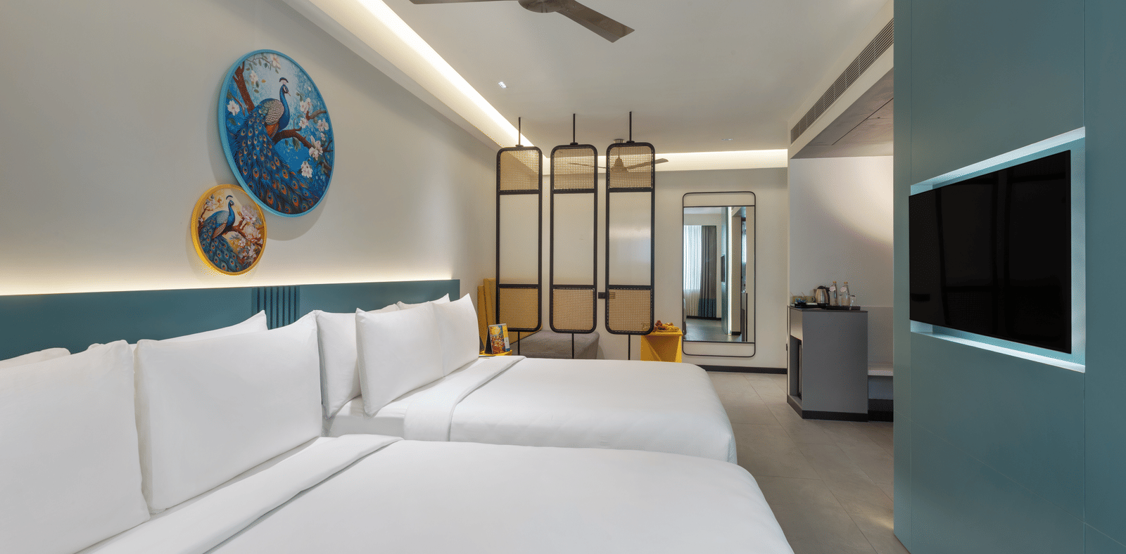 A hotel room with 2 large beds, a wall-mounted TV, a ceiling fan, and a separate seating area making it the best place to stay in Hyderabad for business stays | Zibe Luxe Hyderabad by GRT Hotels