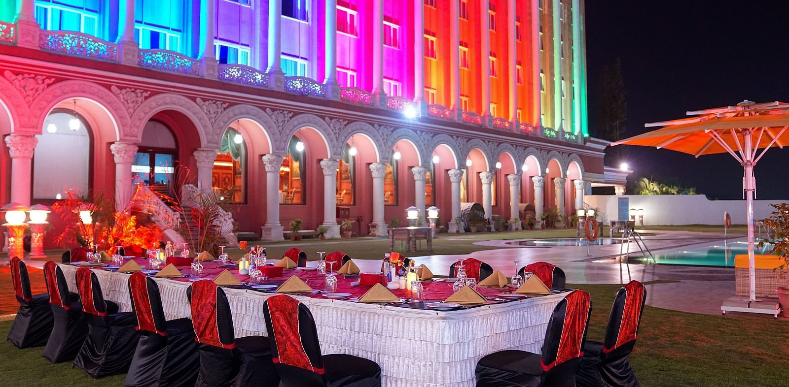 a long banquet table with plates and candles on top of it with Sitara Luxury Hotel in the background - Ramoji Film City Hotels - Hyderabad 