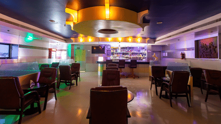 Bar lounge at DSF Grand Plaza, Tuticorin with a circular illuminated ceiling feature, leather chairs around dark tables, and a backlit bottle display.