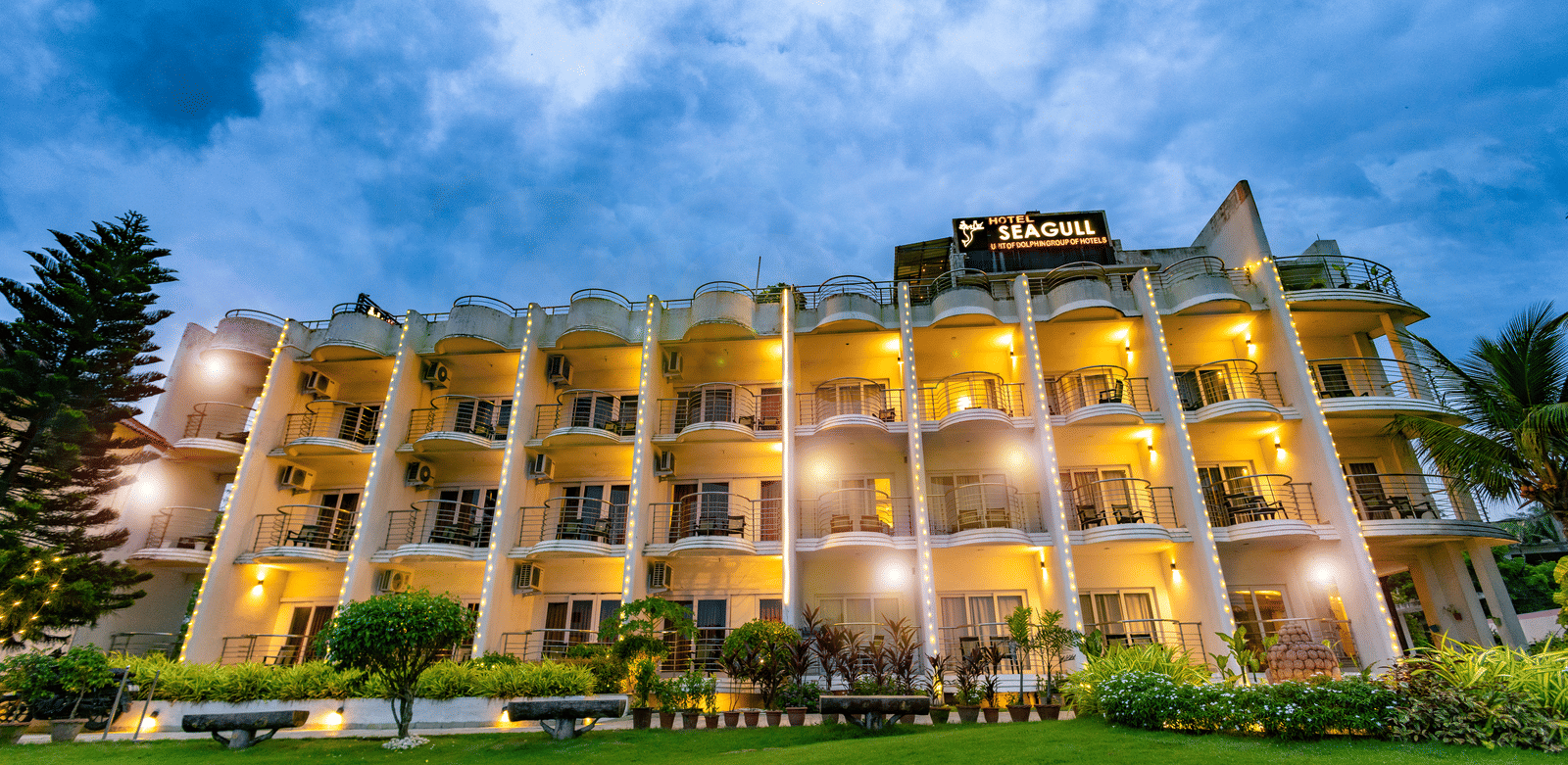 An exterior view of the multi-storey building with balconies and a lawn in front at Hotel Seagull Digha.