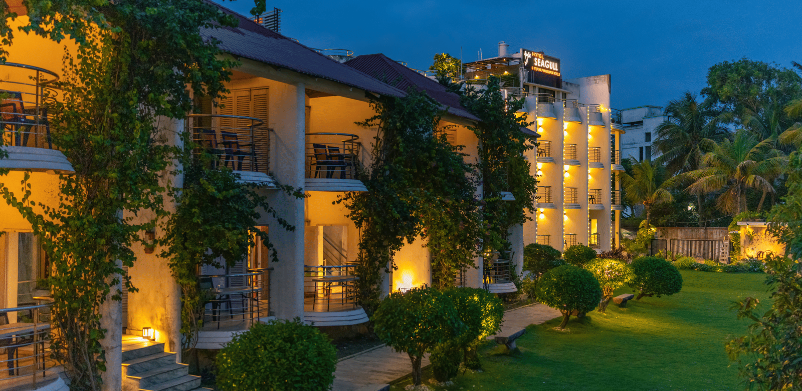 A garden area with pathway, plants, and illuminated building exterior of Hotel Seagull Digha.