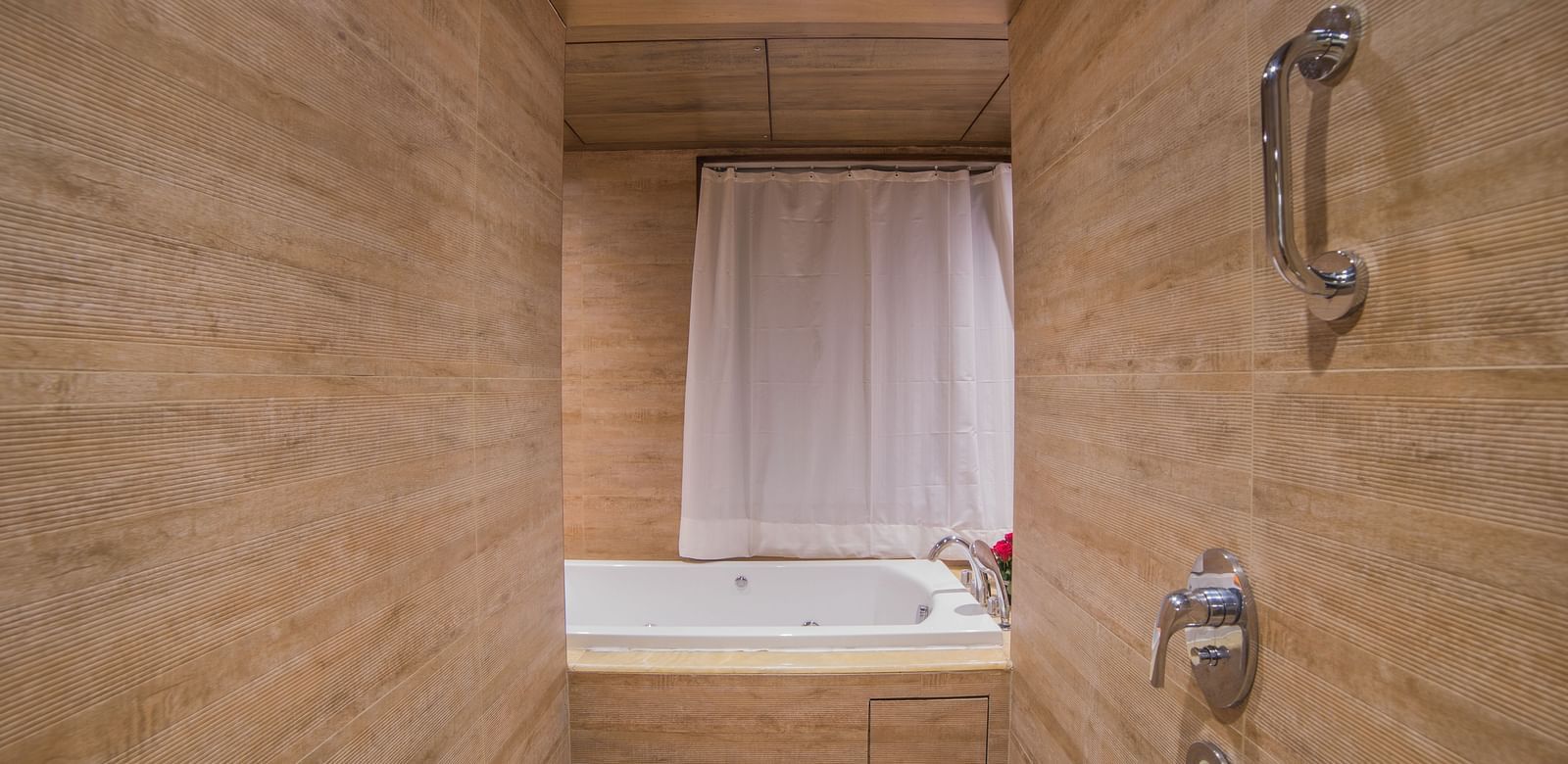 A simple hotel bathroom with a bathtub and shower combination, tiled in beige A grand hotel suite with an opulent red and white decor, large bed, and seating area, reflecting a traditional style at Sitara Luxury Hotel in Hyderabad near Ramoji Film City.