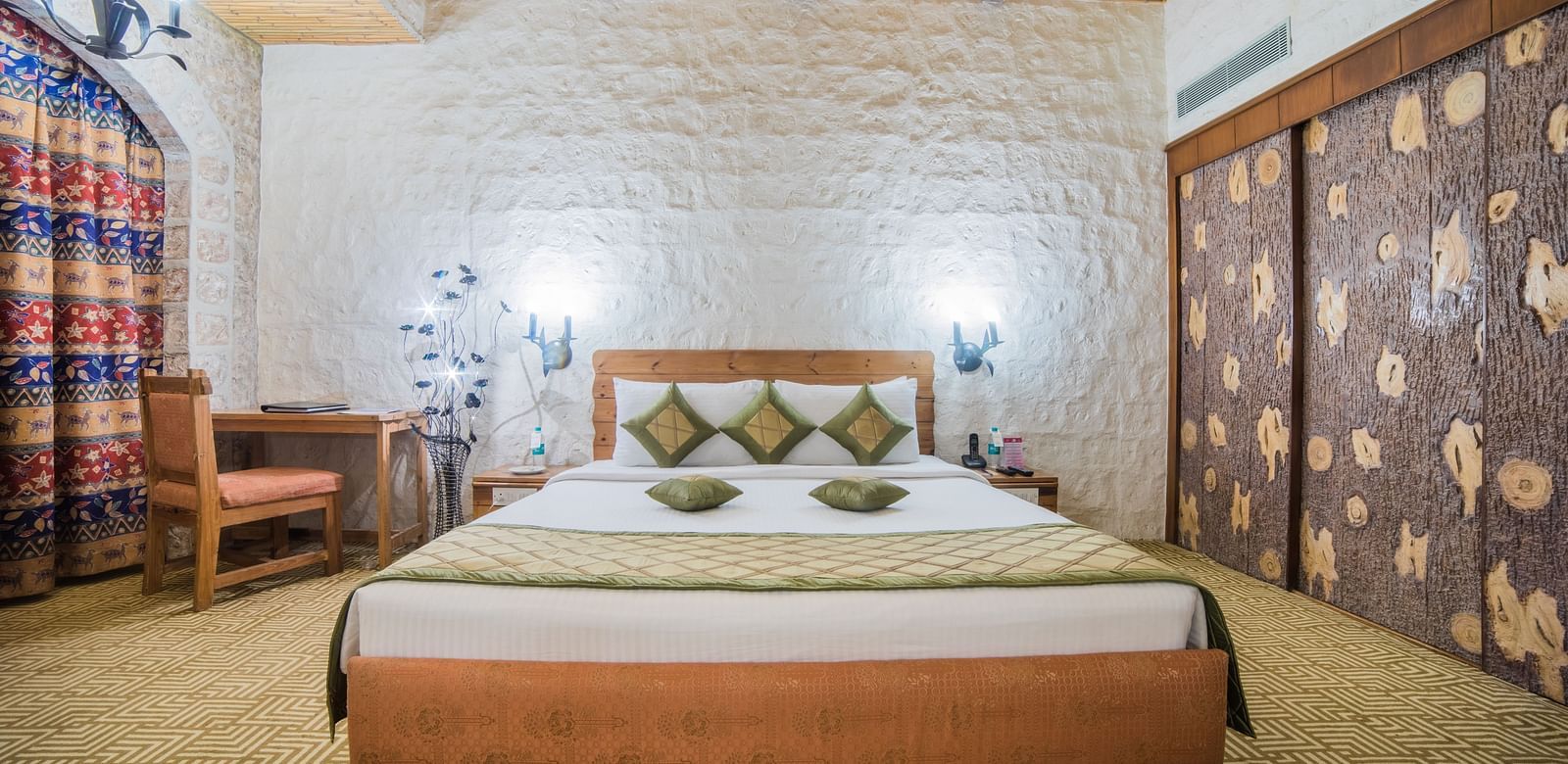 A hotel bedroom with a traditional design, featuring a large bed and stone walls adorned with textile art at Sitara Luxury Hotel in Hyderabad near Ramoji Film City.