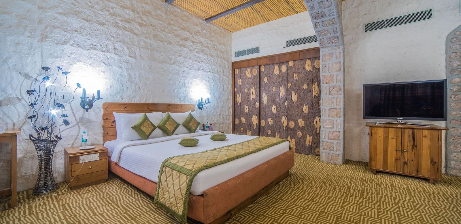 A cozy hotel bedroom with a large bed, wooden accents, and a traditional aesthetic under a vaulted ceiling at  Sitara Luxury Hotel in Hyderabad near Ramoji Film City.