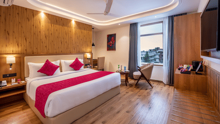 A spacious hotel room at Lords Inn Katra featuring a wide king size bed, a polished wooden wall panel, and a large window overlooking the hills.