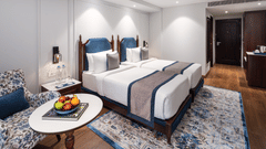 Twin beds with a wooden headboard, a wall-mounted TV, and a round table with a fruit bowl, illuminated by soft cabinet lighting - MJ Sarovar Portico, Haridwar