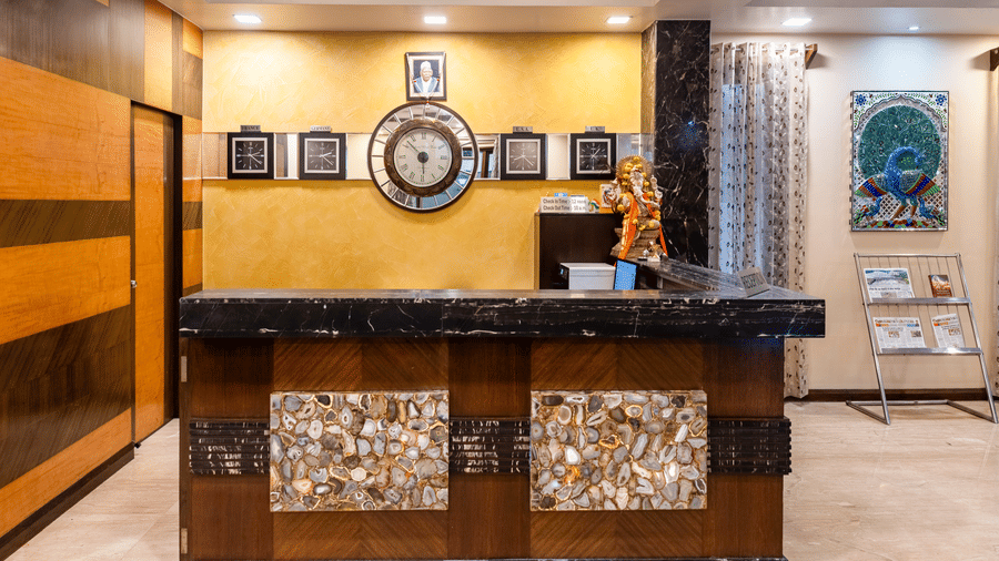 Front view of the reception desk featuring a computer along with a wall-mounted decorative clock - Amantra Comfort Hotel